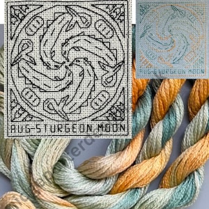 May include: A cross-stitch pattern on white fabric featuring a circular design of four stylized sturgeon fish arranged in a rotating pattern, with geometric corner accents and the text AUG-STURGEON MOON, accompanied by twisted skeins of green and gold embroidery floss.