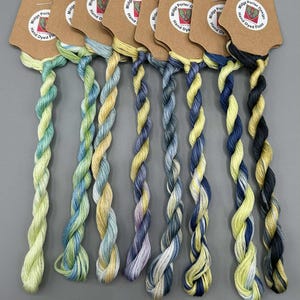 May include: A selection of hand-dyed embroidery floss in a range of two-tone hues. Each skein is attached to a brown tag. The colour scheme features greens, blues, yellows, and purples. The image text reads "Two Tone' Collection 3 of 4."