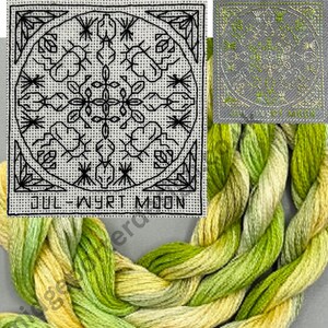 May include: A square cross-stitch pattern on white fabric featuring black geometric and floral motifs with the text JUL-WYRT MOON, accompanied by a braided skein of variegated green and yellow embroidery thread and a small green stitched sample.