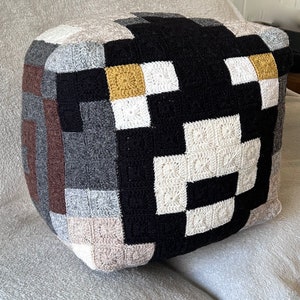 May include: A black, white, brown, and gold crocheted pillow with a pixelated design.
