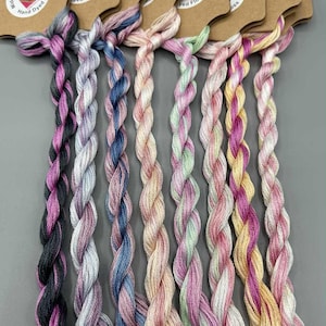 May include: A collection of hand-dyed embroidery floss in pastel shades of pink, purple, blue, and yellow. Each skein is attached to a brown paper tag with the text "Porter Design Hand Dyed Floss". The text "Light Fantastic: Set 4 of 4" is at the bottom.