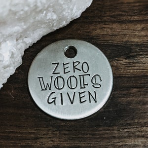May include: A silver metal dog tag with the text "ZERO WOOFS GIVEN" engraved on it.