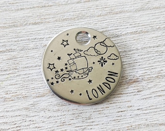 May include: Silver round pet tag with a ship sailing on a starry night with clouds and the word "LONDON" engraved on the tag.