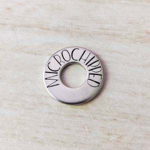 Peut inclure: Une rondelle en métal argenté avec le mot "MICROCHIPPED" gravé sur le bord.