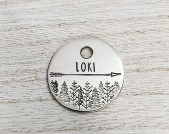 May include: Silver round pet tag with a forest scene and an arrow with the name "Loki" engraved on it.
