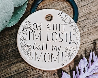 May include: A round, copper-colored keychain with a floral design and the text "Oh Shit I'm Lost! Call my Mom!" engraved on it.