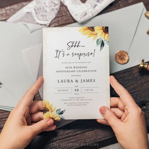 May include: A white invitation card with gold glitter and a watercolor sunflower design. The text reads "Shhh... It's a surprise!" and announces a 50th wedding anniversary celebration for Laura & James on September 19, 2023, at 2:00 PM at the Tribeca Rooftop in New York City.