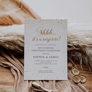 K&ouml;nnte beinhalten: Eine wei&szlig;e Einladungskarte mit goldenem Text und konfettiartigen Punkten. Der Text lautet "Shhh... it's a surprise!" und k&uuml;ndigt eine Feier zum 50. Hochzeitstag zu Ehren von Sophia & James an. Inklusive RSVP-Details.
