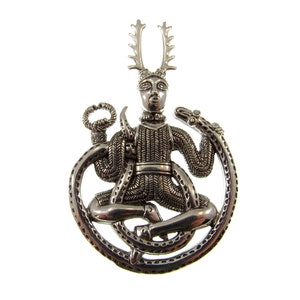 Pu&ograve; includere: Pendente in argento raffigurante una figura cornuta con corna, seduta in un cerchio formato da un serpente. La figura indossa un abito a motivi e ha un viso dettagliato.