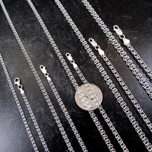 May include: A set of six silver chains of varying lengths, displayed on a black surface. The chains are made of a delicate, interlocking pattern. A US quarter is included for scale.