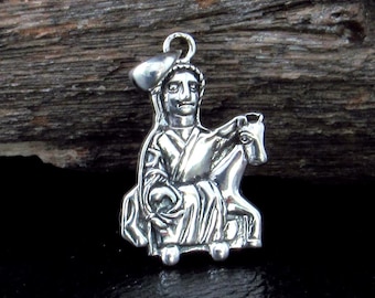 May include: A silver-toned metal pendant featuring a relief design of a figure wearing a cap and robes, seated on a horse. The pendant has a small circular loop at the top for attachment and displays a polished, reflective surface with dark recessed details.
