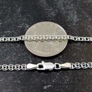 May include: A silver chain necklace with a lobster clasp. The chain is shown next to a US quarter for size comparison.