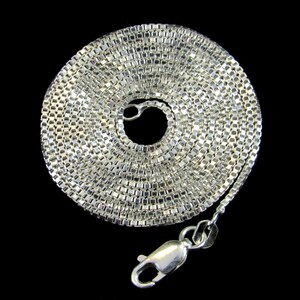 May include: A silver chain necklace with a box chain design. The chain is coiled up and the clasp is visible.