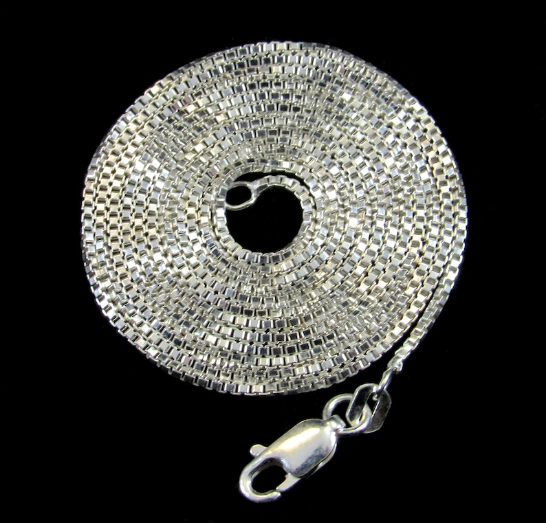 May include: A silver chain necklace with a box chain design. The chain is coiled up and the clasp is visible.