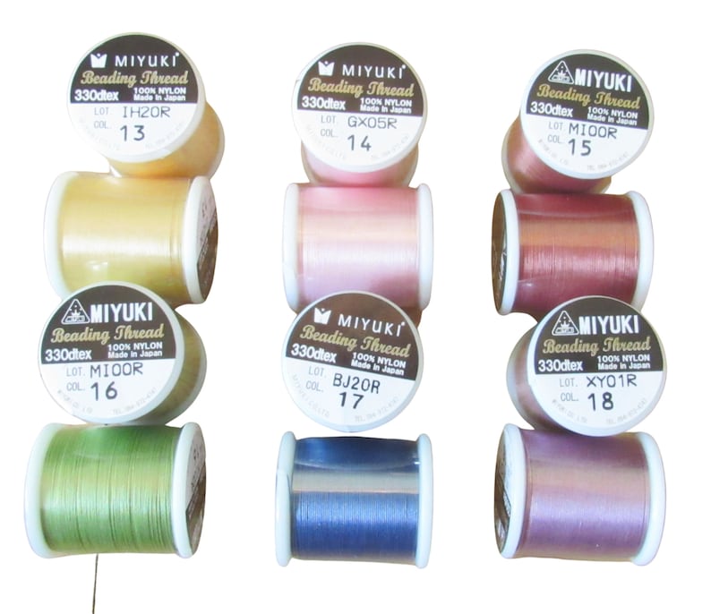 May include: Six spools of Miyuki beading thread in various colors including yellow, pink, dark pink, green, blue, and purple. Each spool is labeled with 330dtex, 100% nylon, Made in Japan, and specific lot and color numbers 13 through 18.