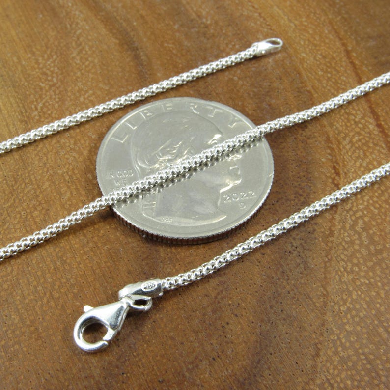 Op de afbeelding: Een zilveren ketting met een karabijn sluiting. De ketting wordt getoond naast een Nederlandse 20 cent munt voor een grootte vergelijking.