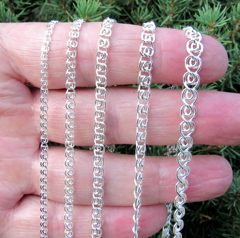 May include: Four silver chains of different widths and lengths, displayed on a hand.