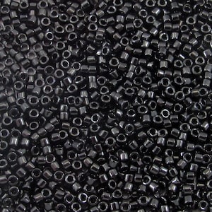 Peut inclure: Gros plan sur une grande quantité de perles de rocaille noires. Les perles sont petites et rondes, avec un trou au centre. Elles sont disposées de manière aléatoire, créant une surface texturée.