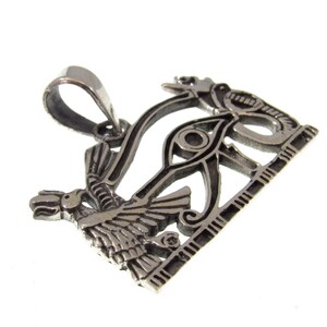 May include: Silver pendant featuring the Eye of Horus, a symbol of protection and good health in ancient Egyptian mythology. The pendant is intricately detailed and features a winged scarab beetle and a cobra.