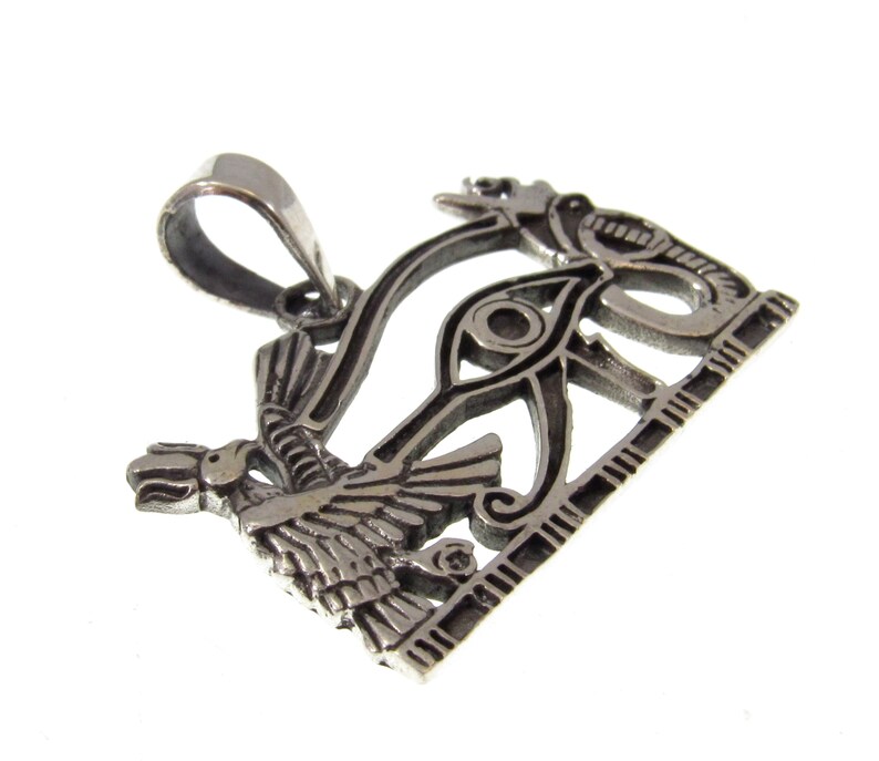 May include: Silver pendant featuring the Eye of Horus, a symbol of protection and good health in ancient Egyptian mythology. The pendant is intricately detailed and features a winged scarab beetle and a cobra.