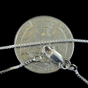 May include: A silver chain necklace with a lobster clasp. The chain is laid on top of a US quarter dollar coin for size reference.