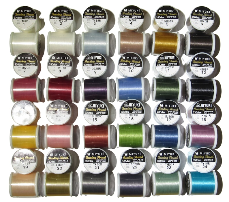 May include: A collection of thirty spools of Miyuki Beading Thread arranged in a grid. Each spool is labeled with the brand name, 330dtex, 100% nylon, and a unique color number. The threads feature a wide variety of solid colors including white, black, red, blue, green, yellow, pink, and metallic tones.