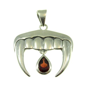 May include: A silver pendant shaped like vampire fangs, with a teardrop-shaped, reddish-brown gemstone hanging from the bottom. The pendant has a loop at the top for a chain.