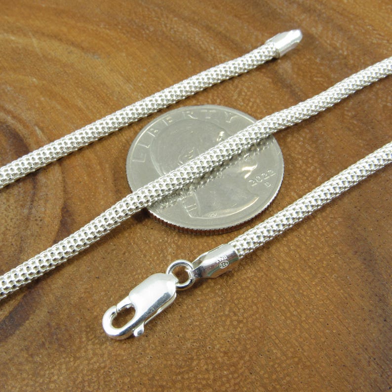 Op de afbeelding: Een zilveren ketting met een getextureerde afwerking. De ketting is ongeveer even breed als een Nederlandse tien-cent munt.