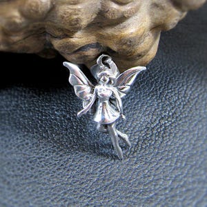 May include: A silver fairy charm with wings and a flowing dress. The charm is detailed and has a delicate design.