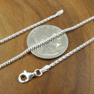 Op de afbeelding: Een zilveren ketting met een karabijn sluiting. De ketting is ongeveer 45 cm lang en wordt getoond naast een Amerikaanse kwart dollar voor een vergelijking van de grootte.