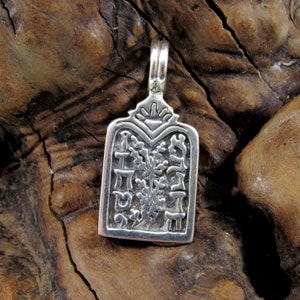 May include: A silver pendant with Hebrew text and floral design. The rectangular pendant has a decorative top with a loop for a chain. The pendant is displayed on a wooden surface.
