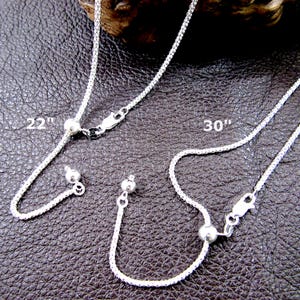 May include: Three silver chain necklaces with adjustable lengths. The chains are 22 inches and 30 inches long. Each chain has a small silver ball at each end.