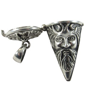 May include: A silver pendant with a triangular Green Man face design. The pendant is open, revealing a detailed floral pattern on the inside. The Green Man has a beard and is surrounded by a laurel wreath.