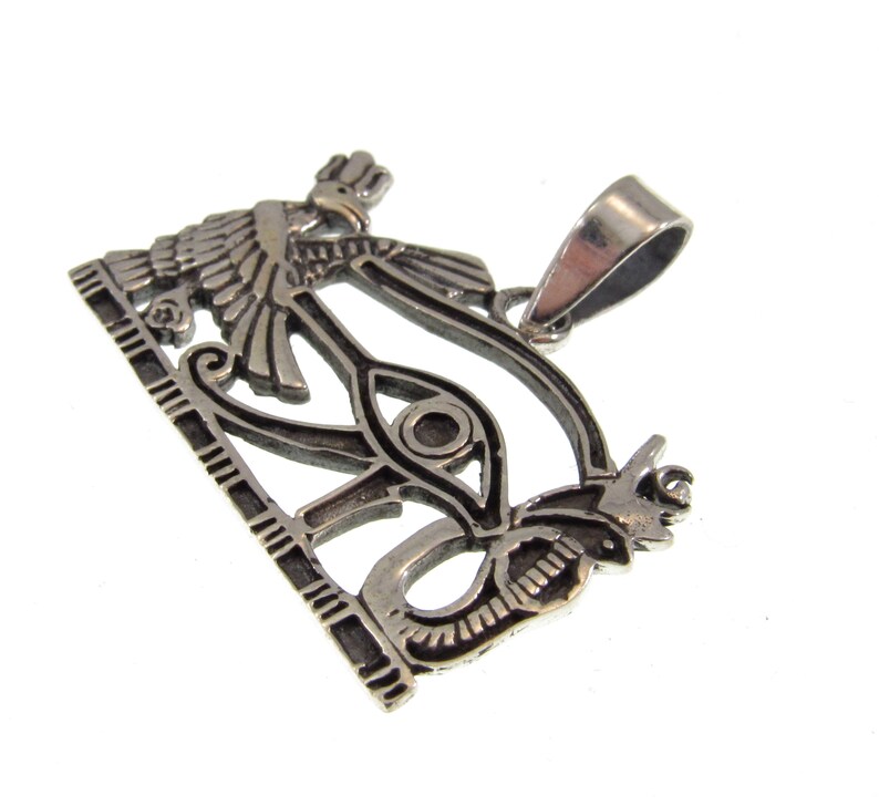 May include: Silver pendant featuring the Eye of Horus, a symbol of protection and good health in ancient Egyptian mythology. The pendant depicts the eye within a winged serpent, with a detailed design and intricate carvings.