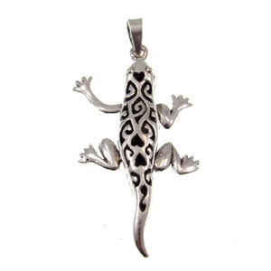 May include: A silver pendant in the shape of a lizard with a detailed, intricate design. The lizard is depicted with a long tail and four legs.