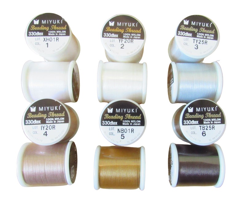 May include: Six spools of Miyuki beading thread arranged in two rows. Each spool is labeled with 330dtex, 100% nylon, and specific lot and color numbers. The threads vary in color, including white, light blue, tan, gold, and dark brown shades.