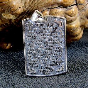 May include: Silver pendant with a rectangular shape and a cross at the top. The pendant is engraved with a prayer in Armenian. The pendant is hanging from a silver chain.