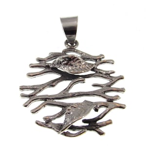 May include: A silver pendant featuring a circular design of intertwining branches with two leaves. The pendant has a loop at the top for attaching a chain.