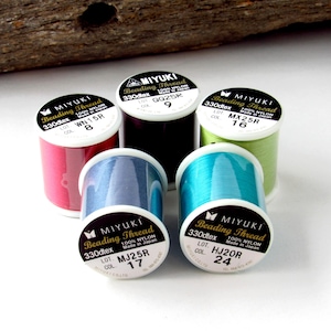 May include: Five spools of Miyuki beading thread made of 100% nylon. The spools are in red, dark purple, light green, blue, and turquoise. Each spool features a white label with black text including the brand name, 330dtex, and color codes.