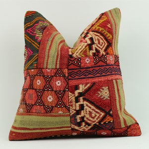 May include: A red, green and black patterned throw pillow with a patchwork design. The pillow is made of woven fabric and has a square shape.