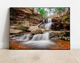 Könnte beinhalten: Eine Langzeitbelichtung eines Wasserfalls, der über Felsen in einem Wald herunterstürzt. Das Wasser fließt sanft und die Felsen sind mit Moos und Blättern bedeckt. Der Wald ist üppig und grün, mit Bäumen auf beiden Seiten des Wasserfalls.