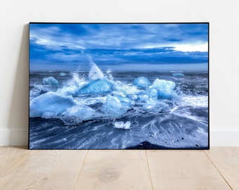 May include: A framed print of a coastal scene featuring icebergs and ocean waves. The image is dominated by shades of blue, with the sky, water, and icebergs creating a cool, serene atmosphere. The black frame adds a modern touch to the artwork.