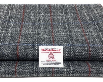 Op de afbeelding: Twee gevouwen stukken grijze Harris Tweed stof met een ruitpatroon. De stof heeft rode en blauwe strepen. Een wit label met het Harris Tweed logo en tekst is zichtbaar.