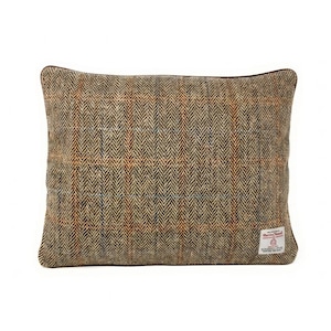 May include: A square throw pillow featuring a brown, tan, and orange herringbone tweed fabric with a subtle plaid pattern. A small white rectangular label with red and black text is stitched onto the bottom right corner of the pillow cover.