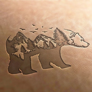 Peut inclure: Un fond en cuir brun avec une silhouette d'ours avec des montagnes et des oiseaux à l'intérieur du contour de l'ours.