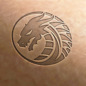 Puede incluir: Un diseño de cabeza de dragón en blanco y negro está tallado en un trozo circular de cuero marrón.