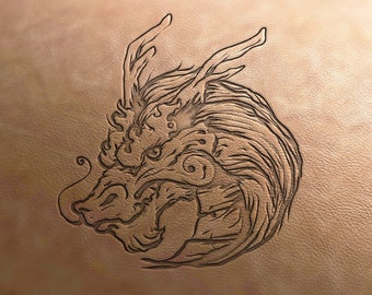 Op de afbeelding: Een gedetailleerde lijntekening van een drakenkop, gegraveerd in een stuk leer. Het gezicht van de draak is fel en krachtig, met scherpe tanden en hoorns.