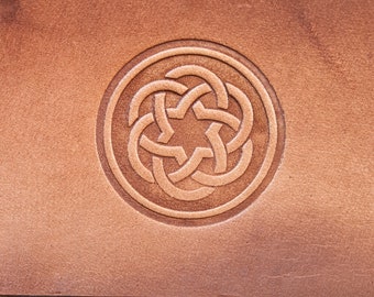 Könnte beinhalten: Nahaufnahme eines braunen Lederflicken mit einem runden Design, das in die Oberfläche geprägt ist. Das Design zeigt einen fünfzackigen Stern, der von einem keltischen Knotenmuster umgeben ist.