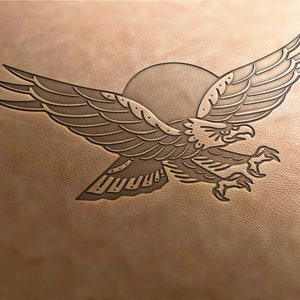 May include: A brown leather background with a black and white eagle tattoo design. The eagle is flying with its wings spread and has a sun behind it.