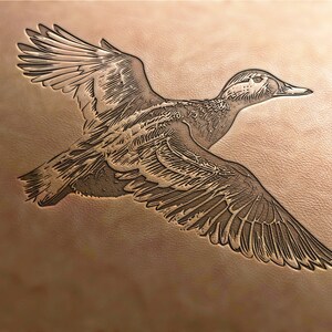 Könnte beinhalten: Ein detailliertes, geprägtes Bild eines fliegenden Enten, in ein Stück Leder geschnitzt. Die Ente ist braun und weiß mit einem langen, spitzen Schnabel.